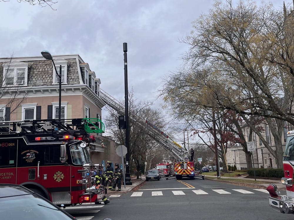 Two red fire trucks are in the foreground while another is in the distance. The fire truck in the back is raising a ladder to the top of a cream-colored building.