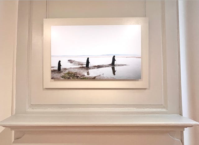 Photograph of three figures in black cloaks walking on sand.