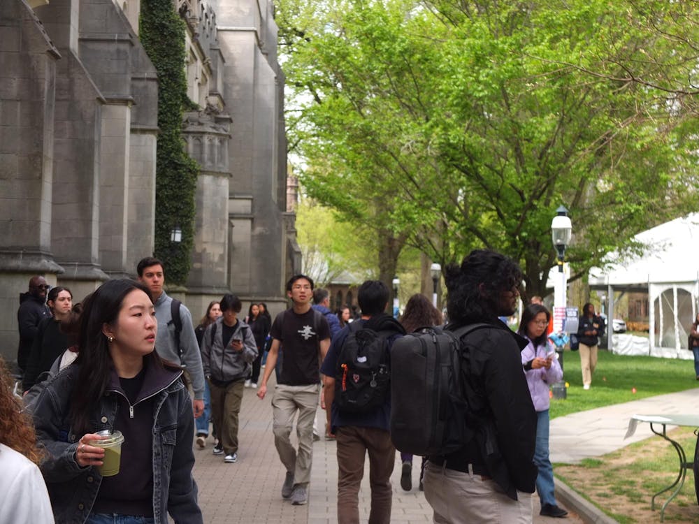 Students on a walkway turn their heads to the right, looking toward a green space.
