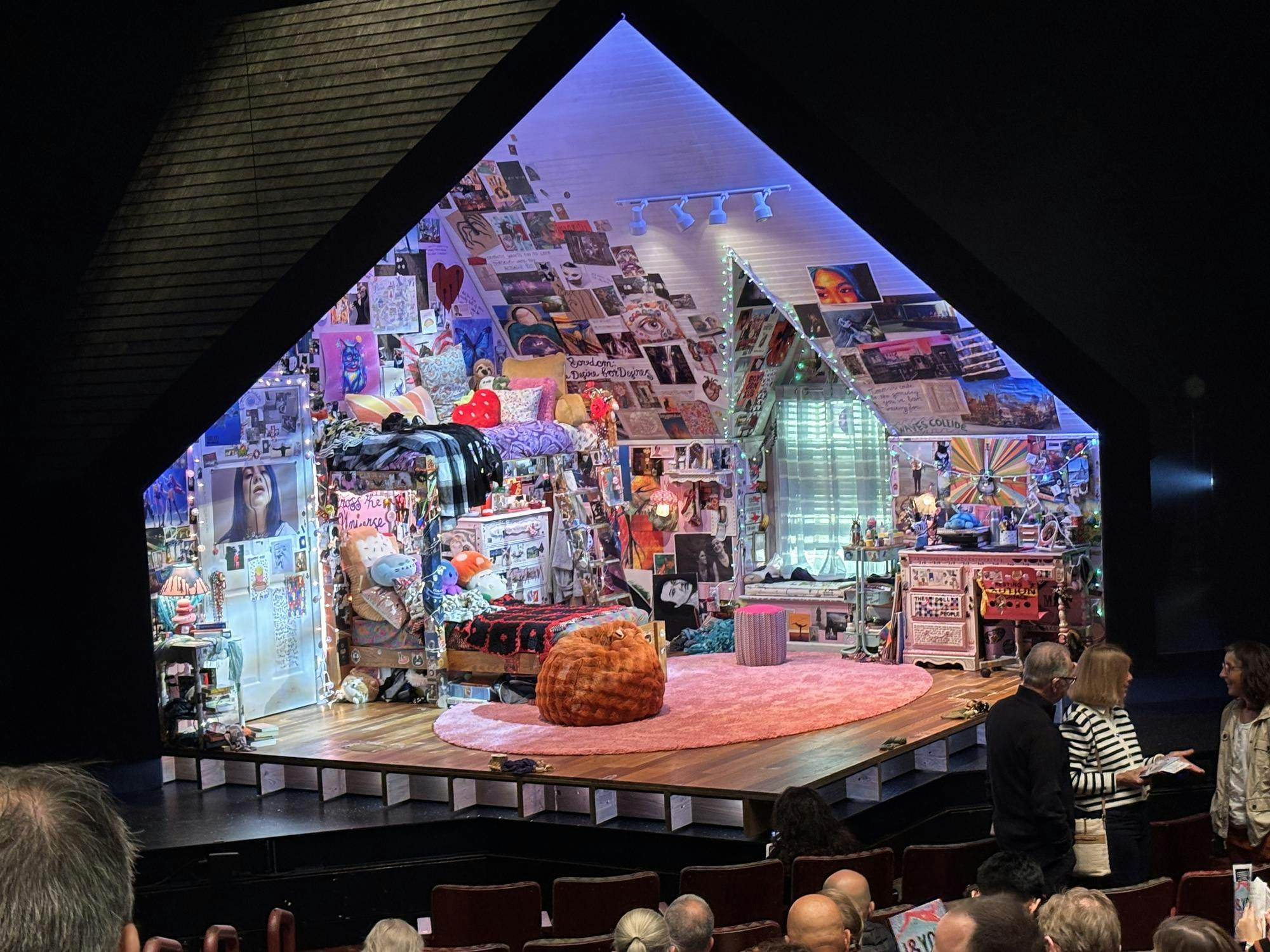 A bedroom covered with colorful posters and paintings of blue, red and pink, sits on a stage which resembles a house. 