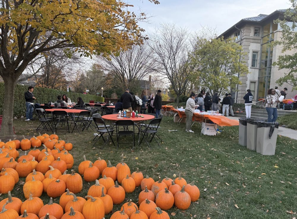 Pumpkins on the ground in front of tables where some people are gathered.