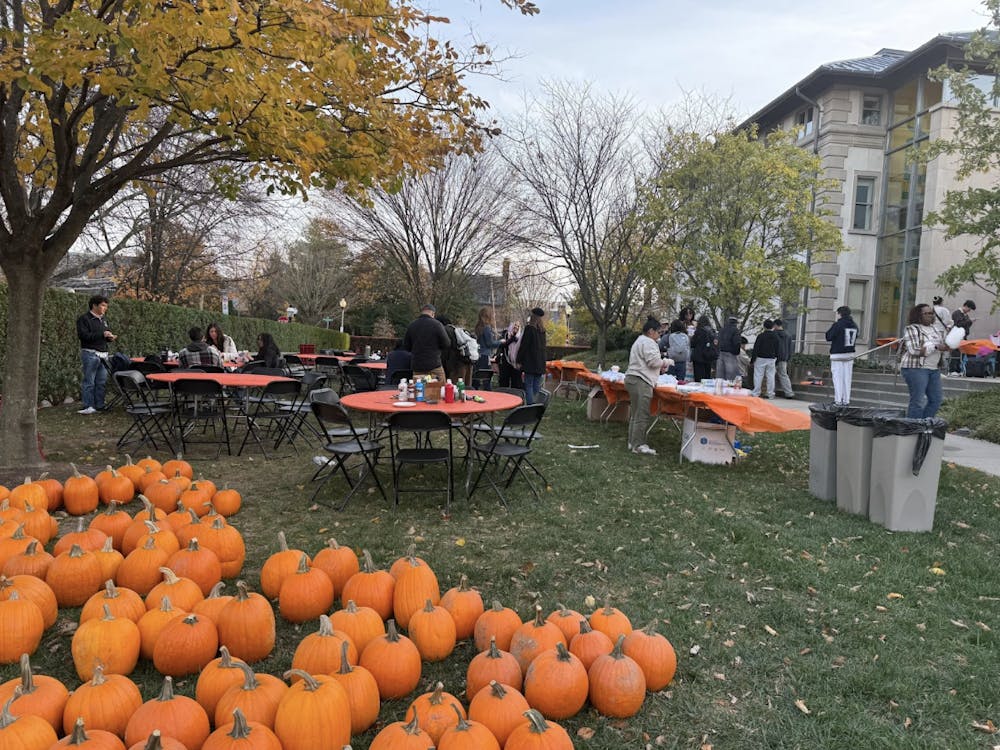 Pumpkins on the ground in front of tables where some people are gathered.