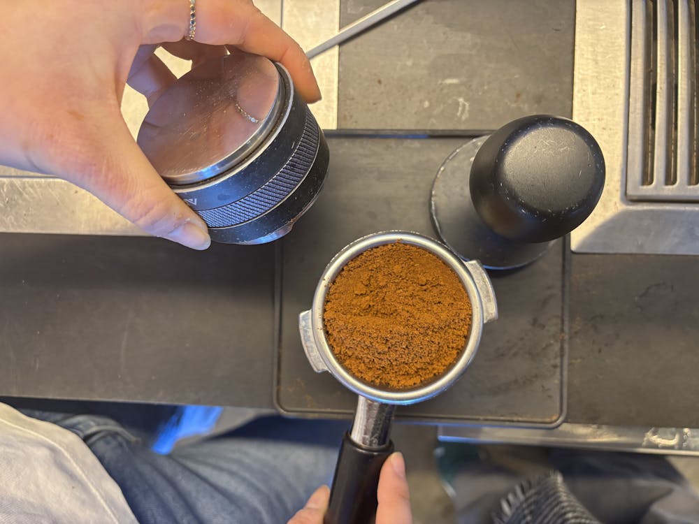 A pair of hands adding a puck of coffee grounds to a portafilter over a coffee machine.