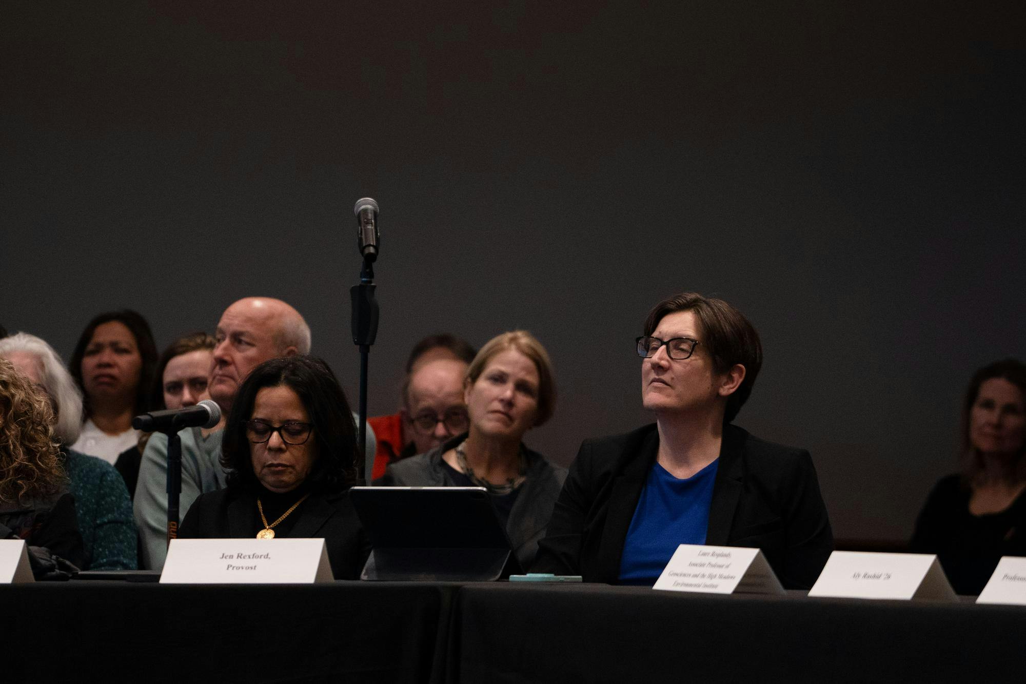 A woman sitting at a table with a placard in front of her at a meeting.