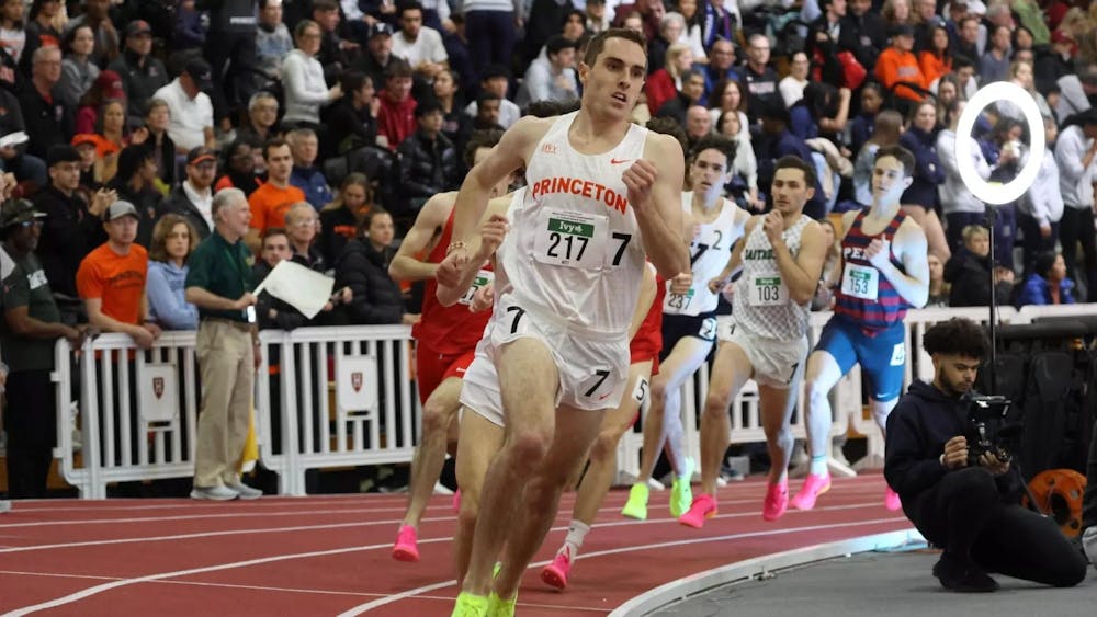 Man in white uniform running ahead of other men wearing a variety of colorful uniforms on a reddish brown track.