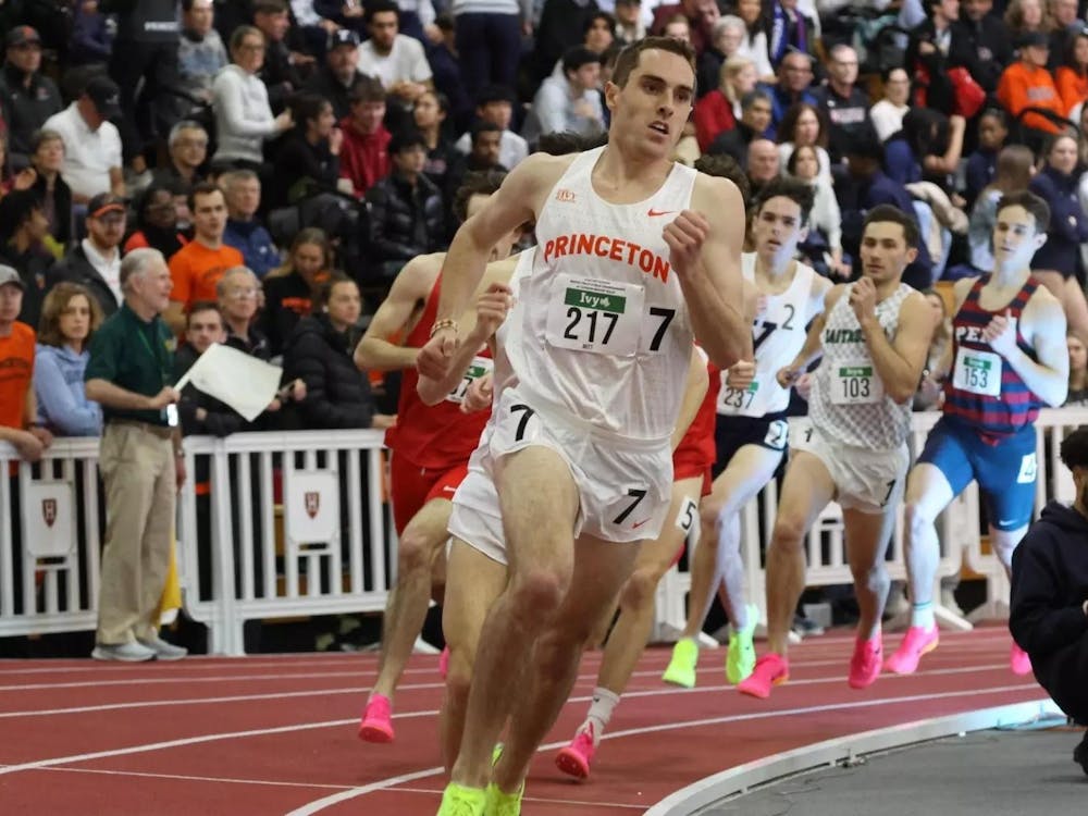 Man in white uniform running ahead of other men wearing a variety of colorful uniforms on a reddish brown track.