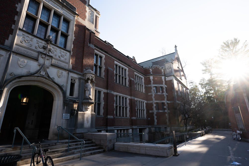 A large brick building with an arched stone doorway in the left and sunlight streaming though the top right corner