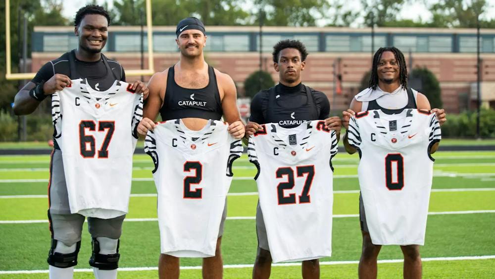 Four football players hold white jerseys with their numbers on them. 