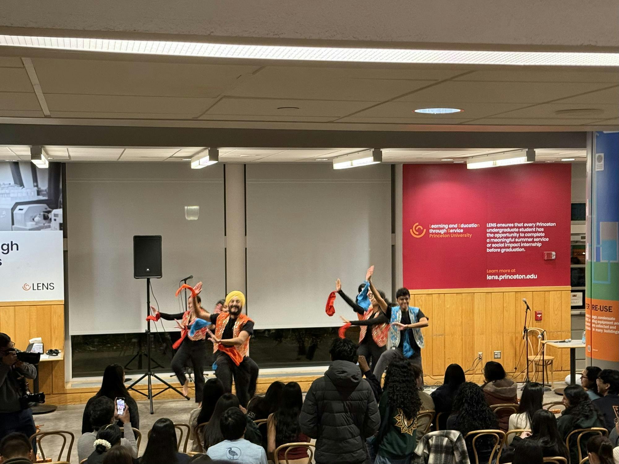 Students perform a dance onstage in front of an audience at a campus event.