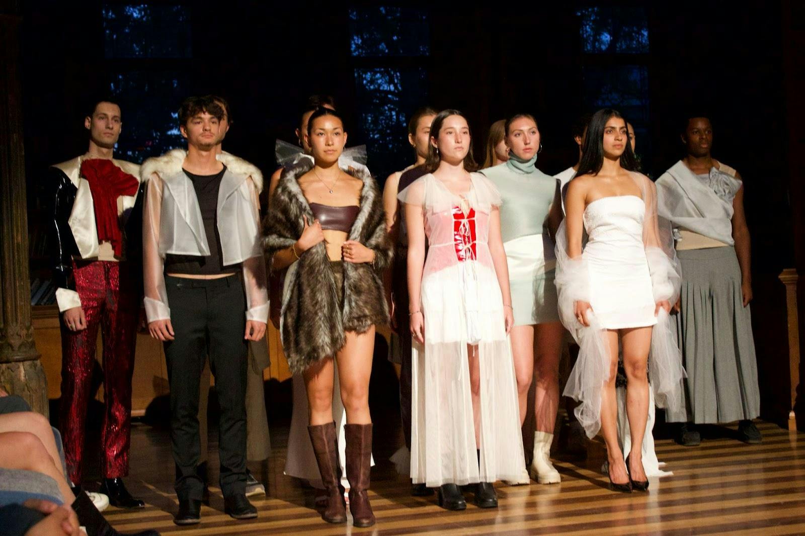 Young men and women dressed in avant-garde outfits and fabrics stand in a pyramid formation behind one another, as they pose at the end of the rotunda or the runway. 
