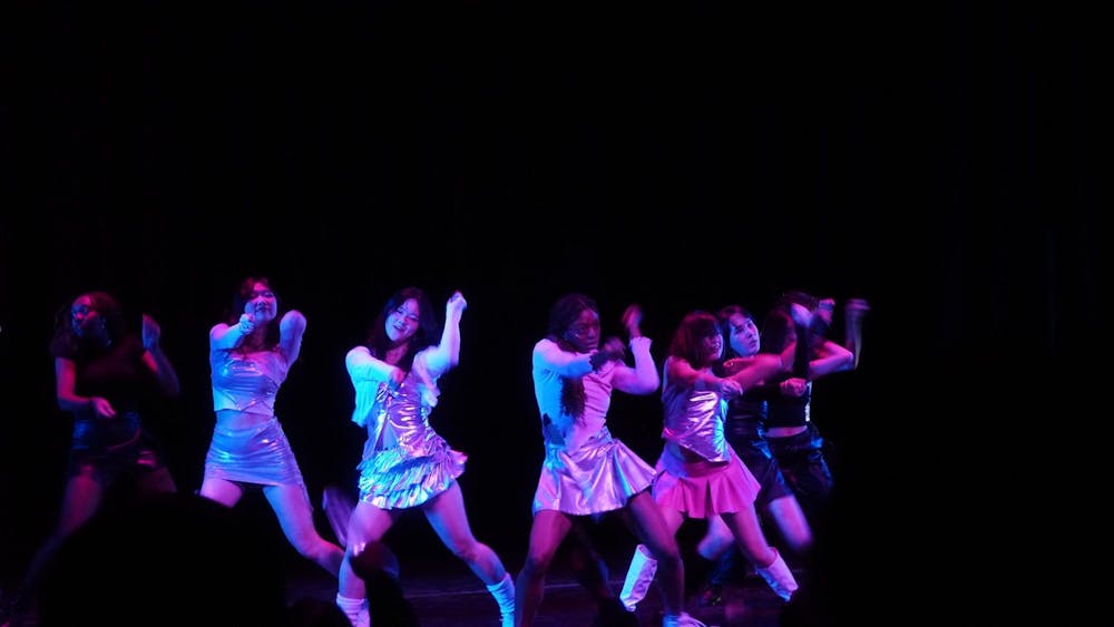 Dancers performing on stage in metallic clothing, under bright, colorful lighting.