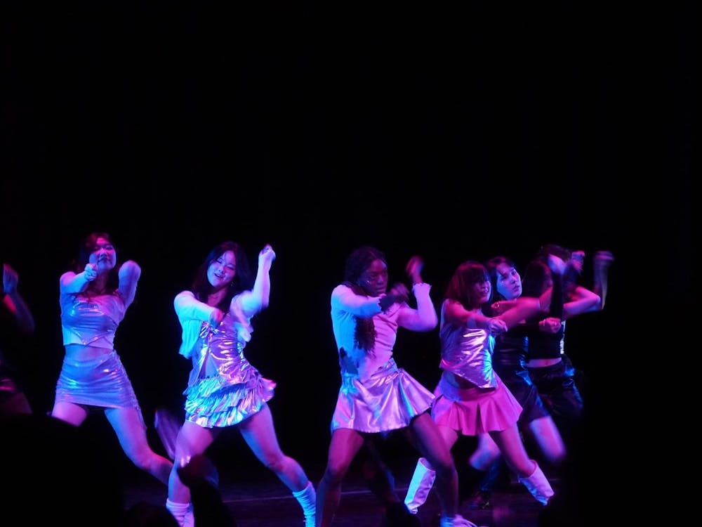 Dancers performing on stage in metallic clothing, under bright, colorful lighting.
