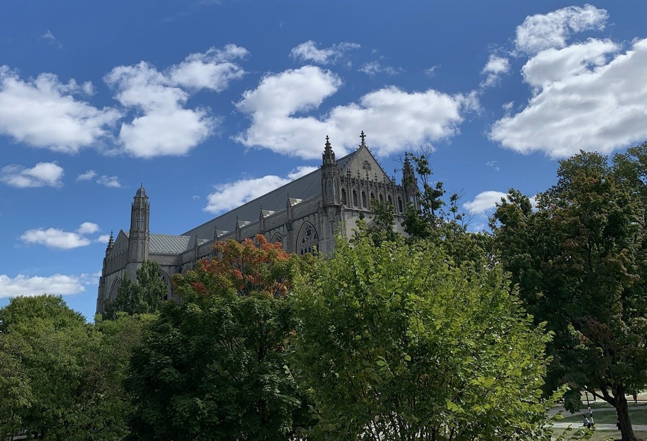 The University chapel with gothic spires behind lush trees and a blue sky. 
