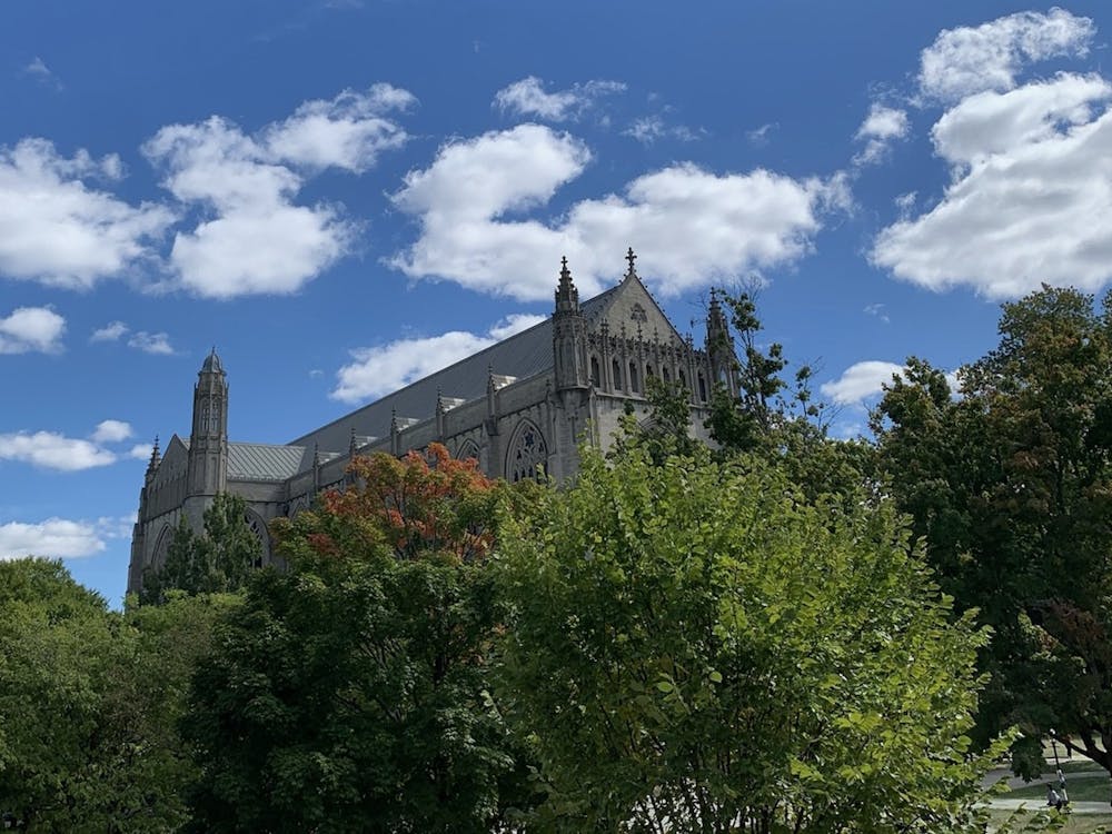 The University chapel with gothic spires behind lush trees and a blue sky. 