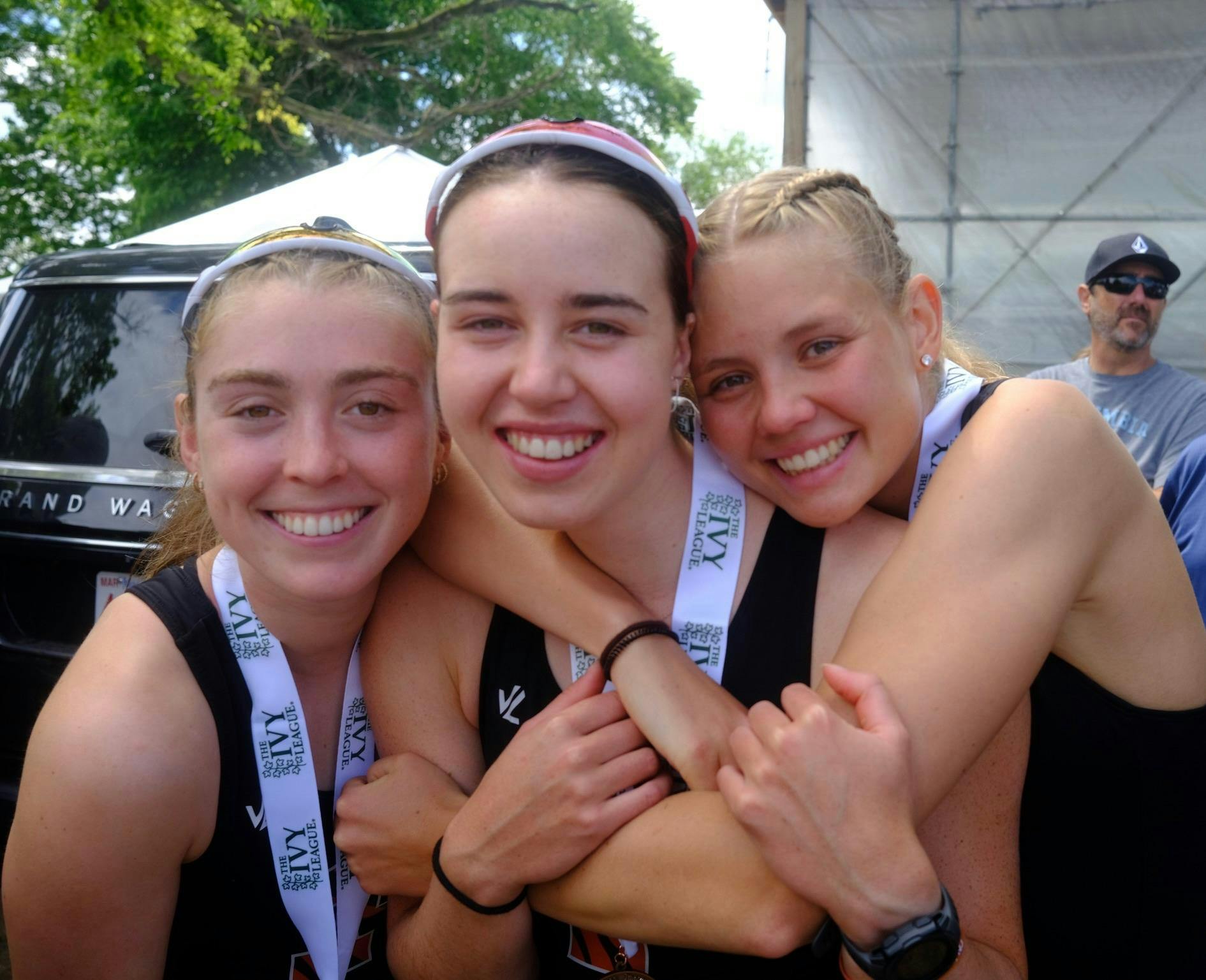 Three women embracing each other while wearing an Ivy League medal. 