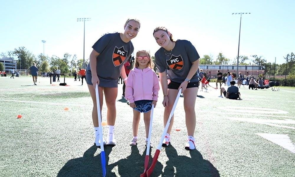Dos atletas de hockey de campo están a cada lado de una atleta joven.