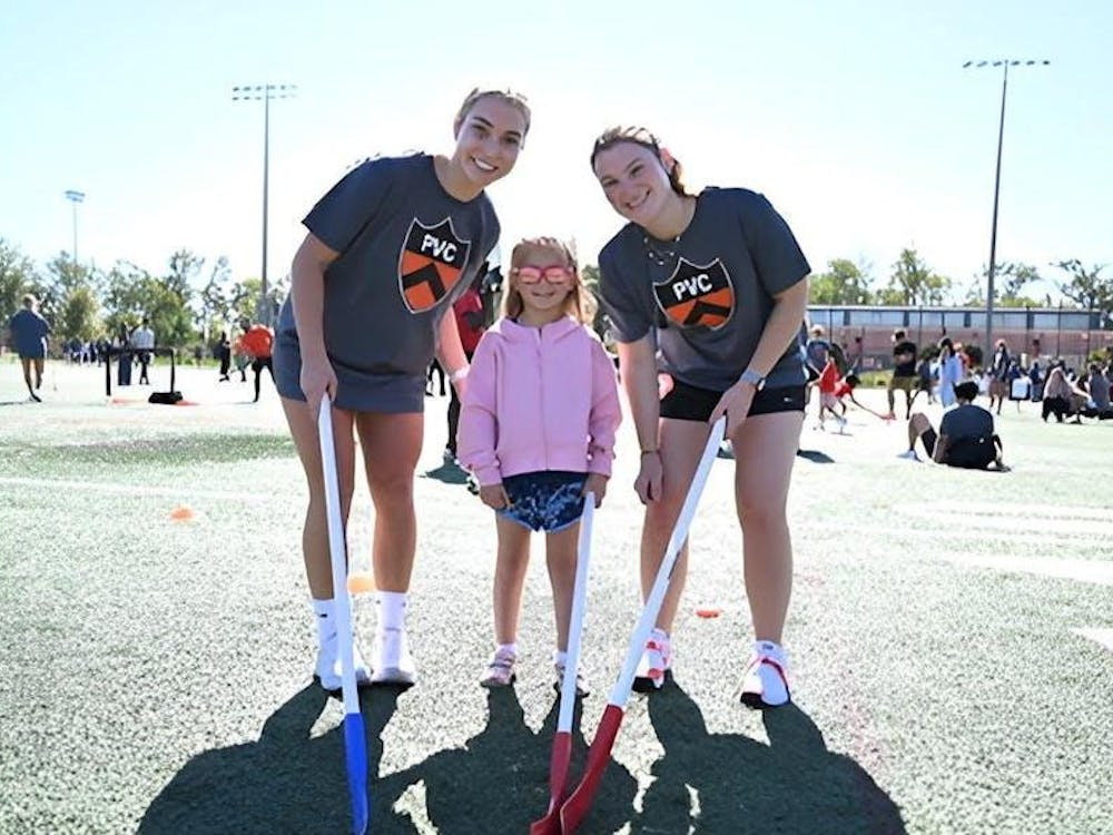 Dos atletas de hockey de campo están a cada lado de una atleta joven.