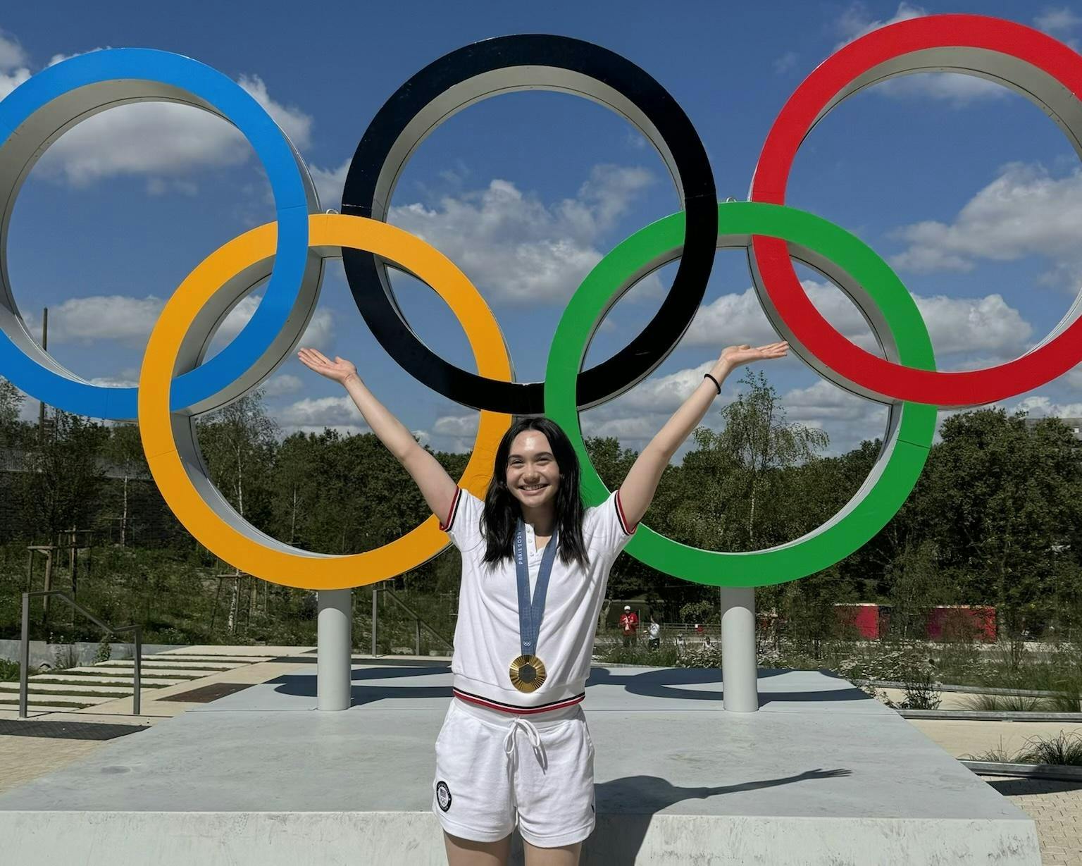 Woman stands in front of Olympic rings.