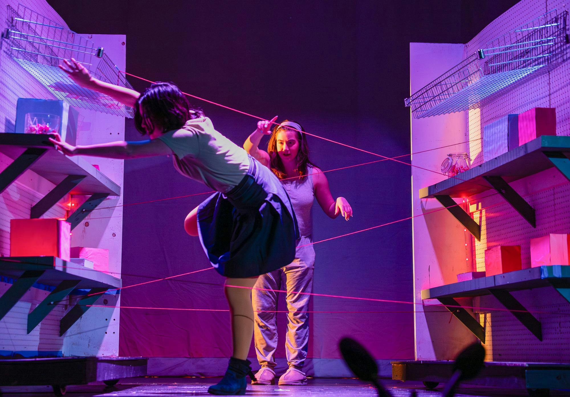 A person tries to navigate through outstretched strings while another person stands further back and guides them.