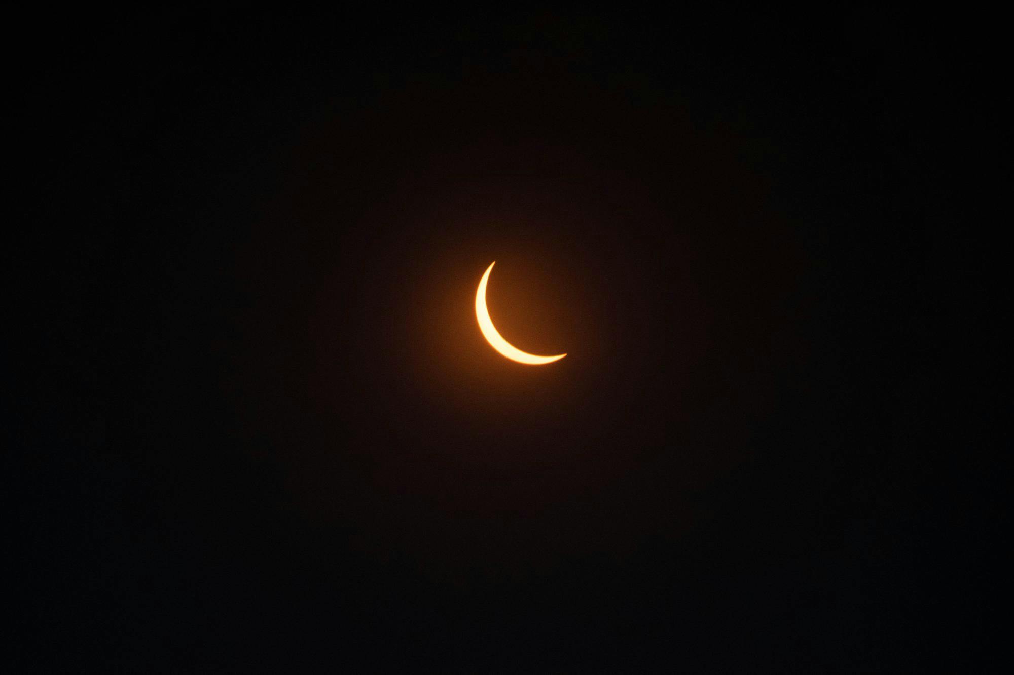 The moon covers nearly all of the sun, appearing as black darkness with a crescent sliver of orange glow showing.