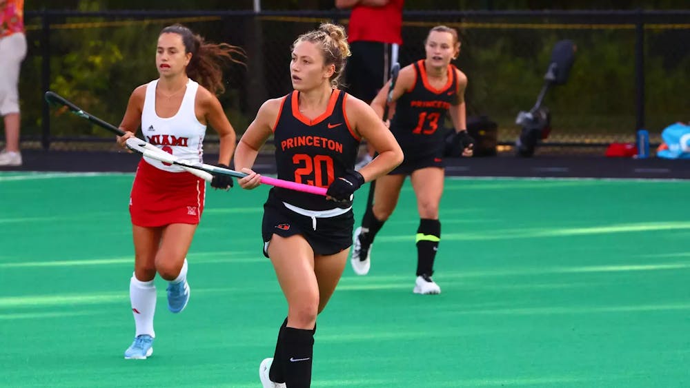 Princeton field hockey player wearing number twenty is carrying a field hockey stick with a pink handle.
