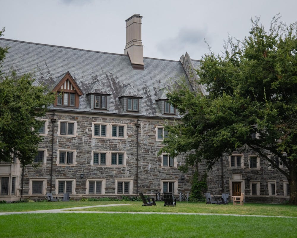gray stone building with triangular roofs behind a courtyard with green grass under an overcast sky