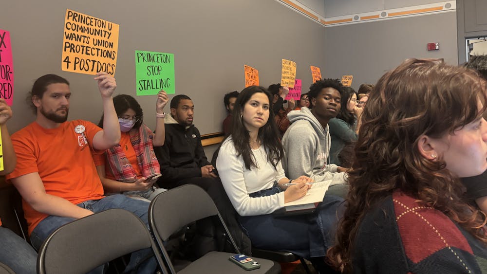 A group of people sitting in an audience in a room with grey walls, holding multicolored signs up.