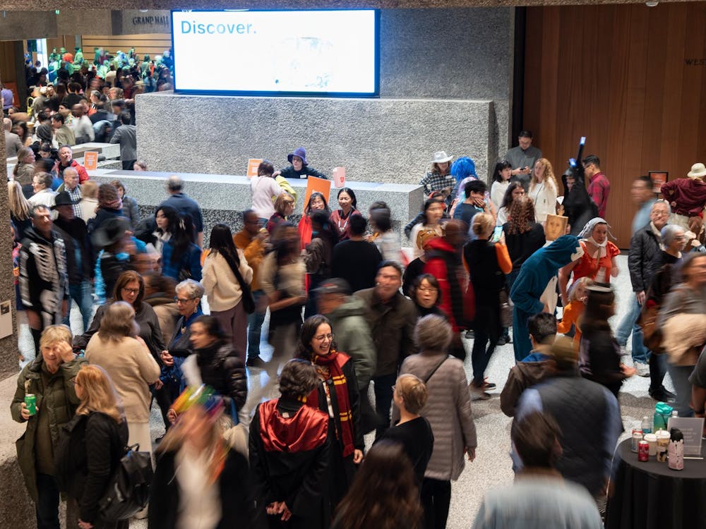 A cluster of people in Halloween costumes mill around a large hallway.