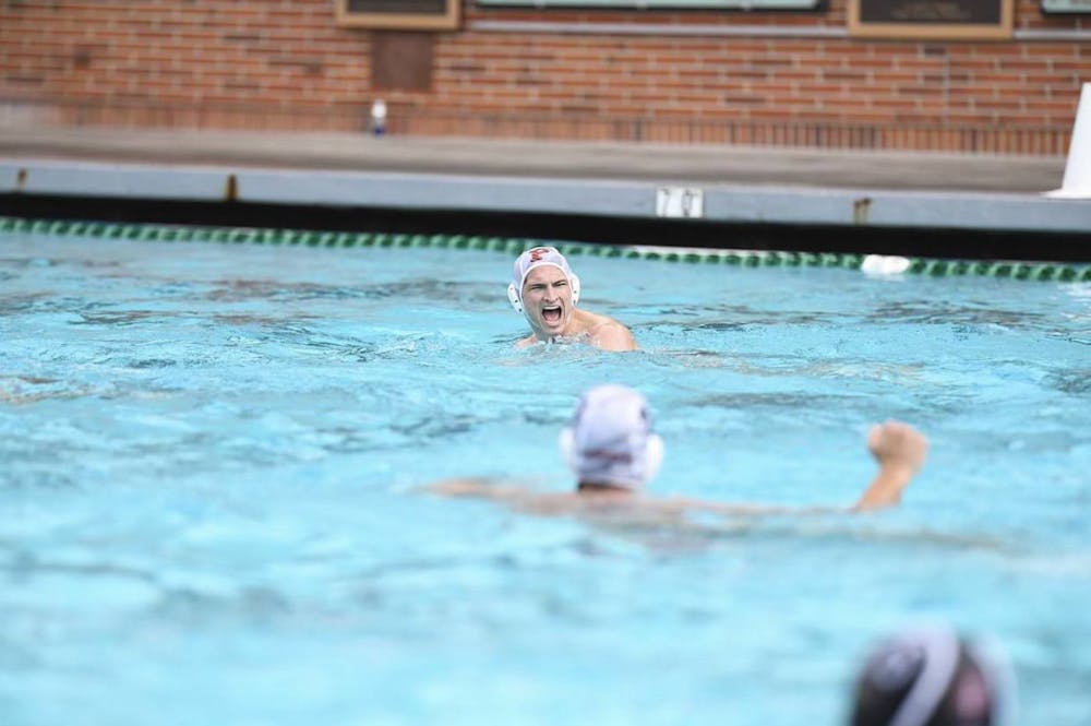 A man in a white cap, swimming with his head visible just above water, yells in excitement.