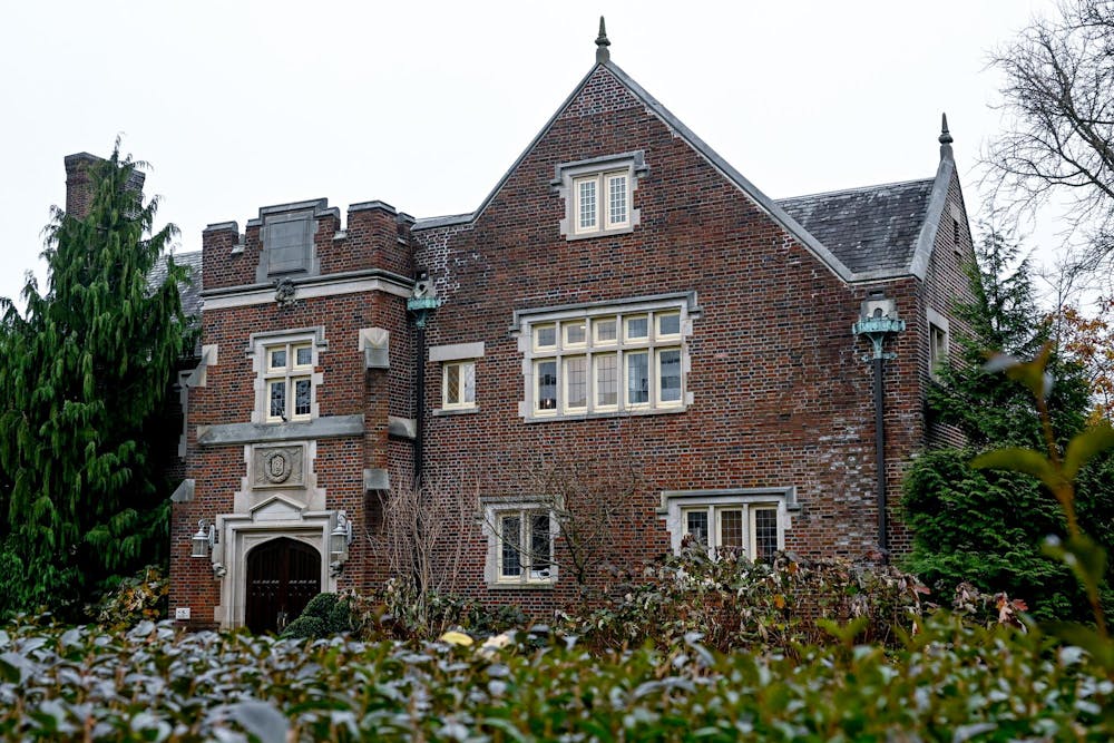 An old brick building looms over bushes. 