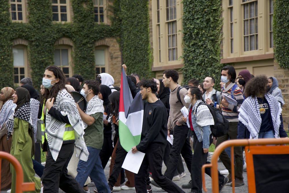 A group of protestors march in front of a building with ivy.