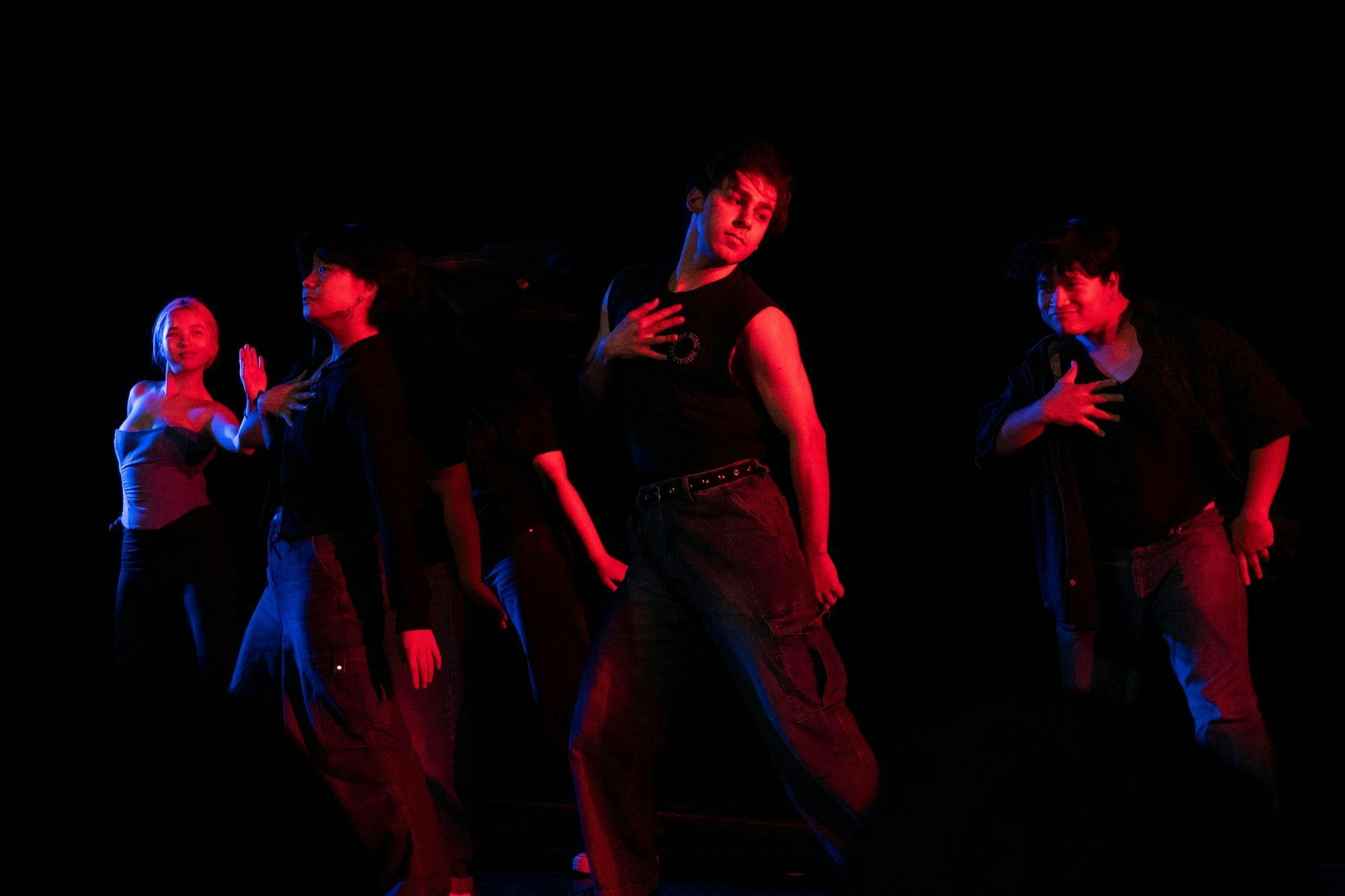 Four dancers perform beneath red lighting.