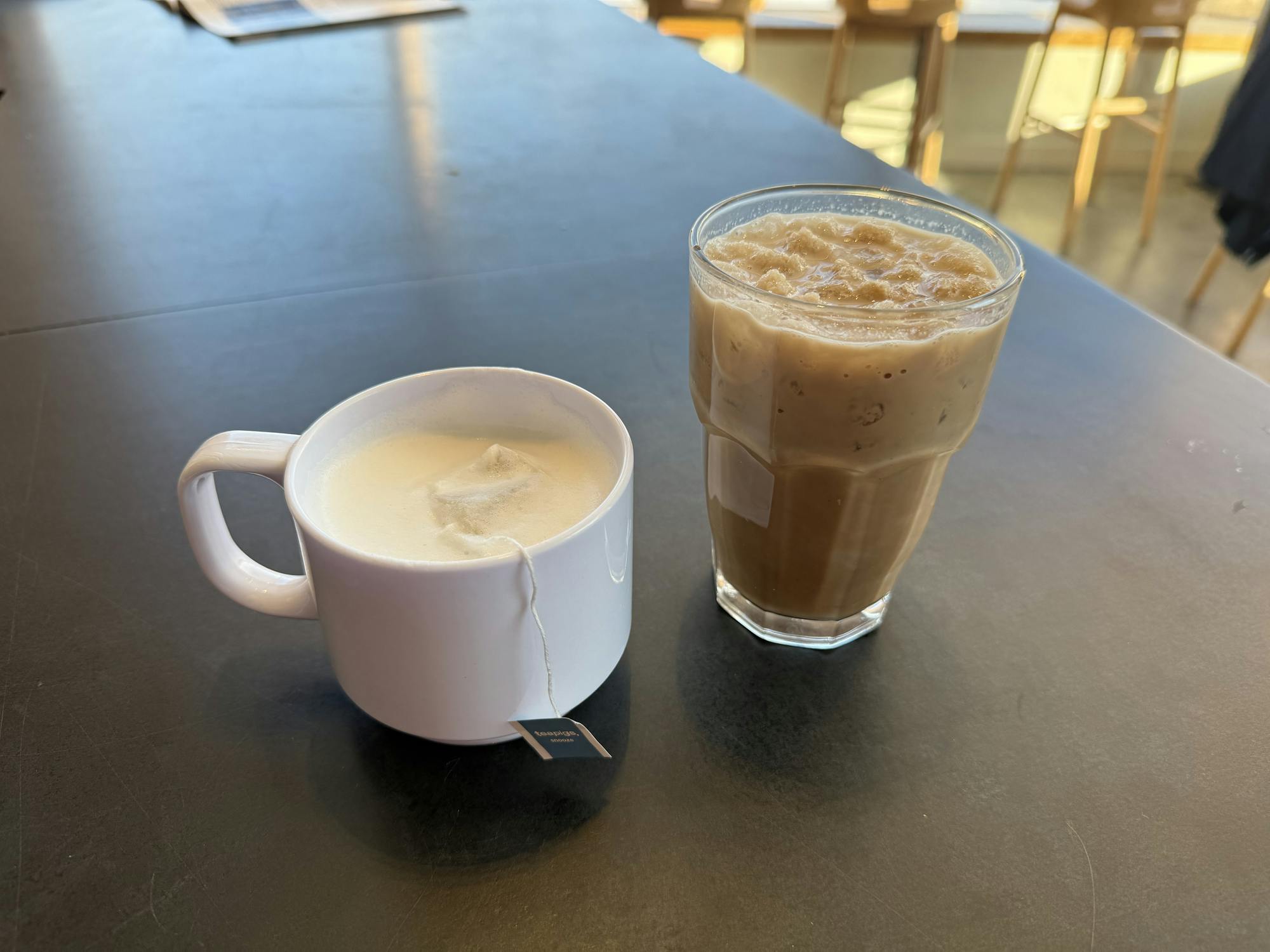 A white coffee mug with a foamy drink and a glass cup filled with coffee sits on a table.