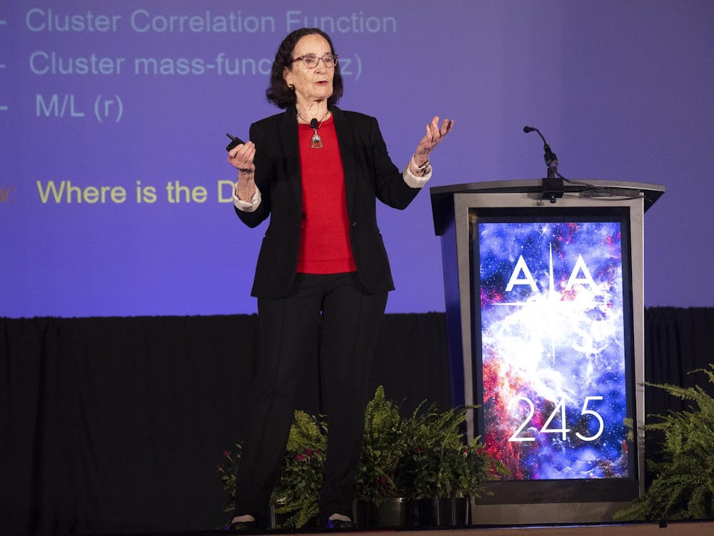 Person in red shirt, black pants and jacket in front of large blue screen.