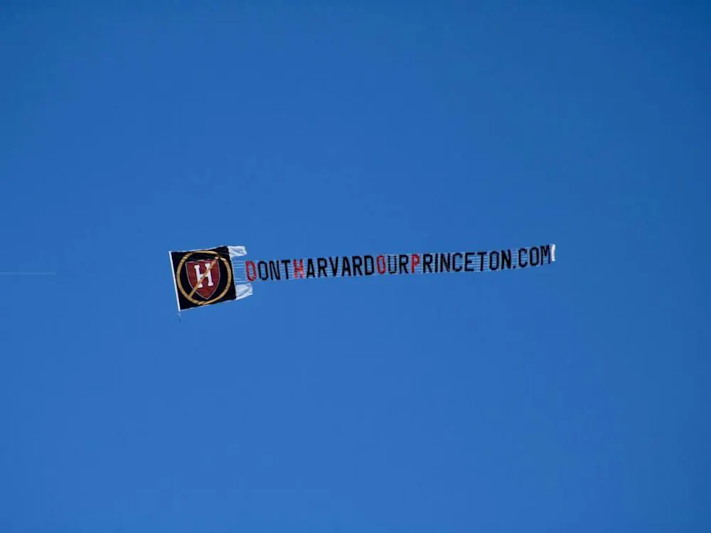 A photograph of the sky with a flying banner reading, “DontHarvardOurPrinceton.com”