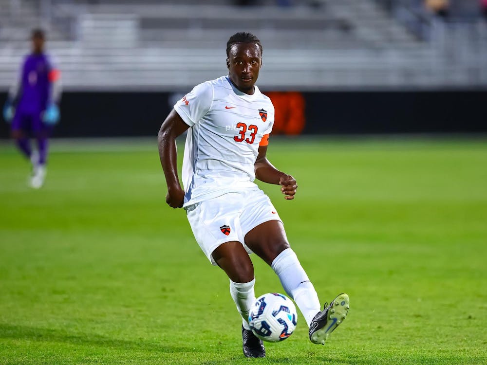 A man wearing white shorts and a white jersey with the number 33, a Nike logo, and a patch all in orange on the jersey on a soccer field kicking a soccer ball.