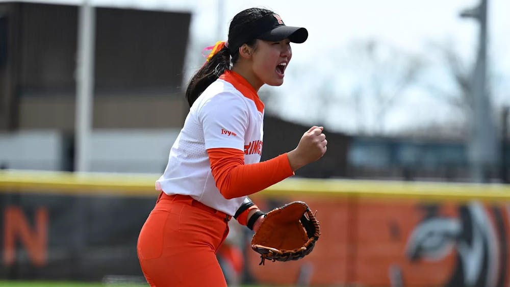 A woman celebrates on a softball field in an orange and white uniform.