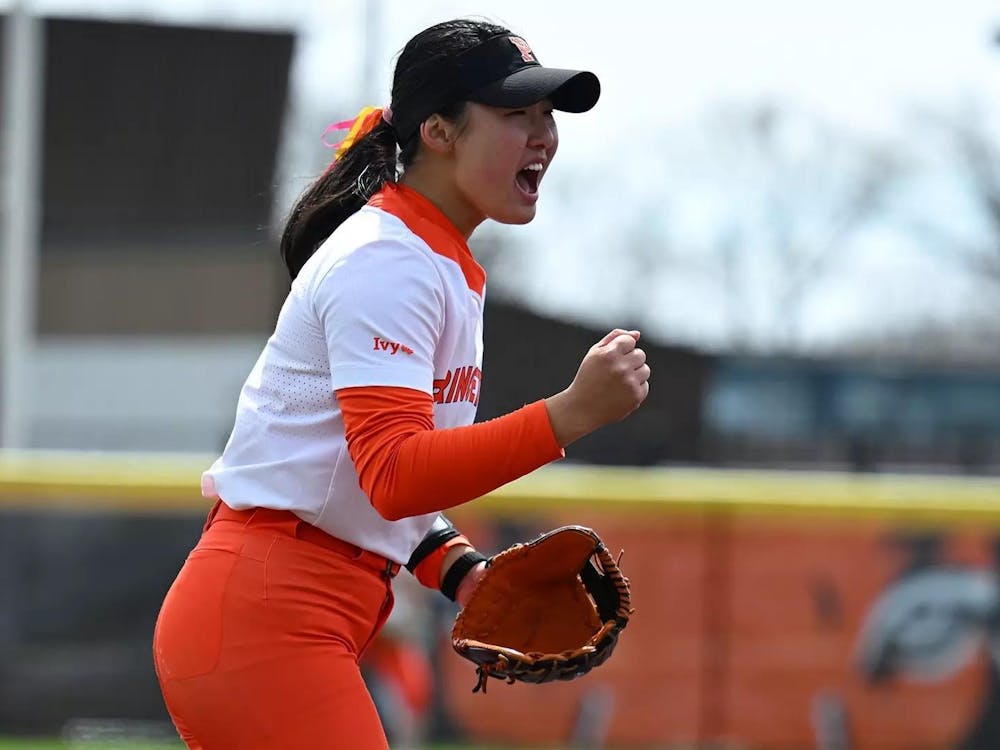 A woman celebrates on a softball field in an orange and white uniform.