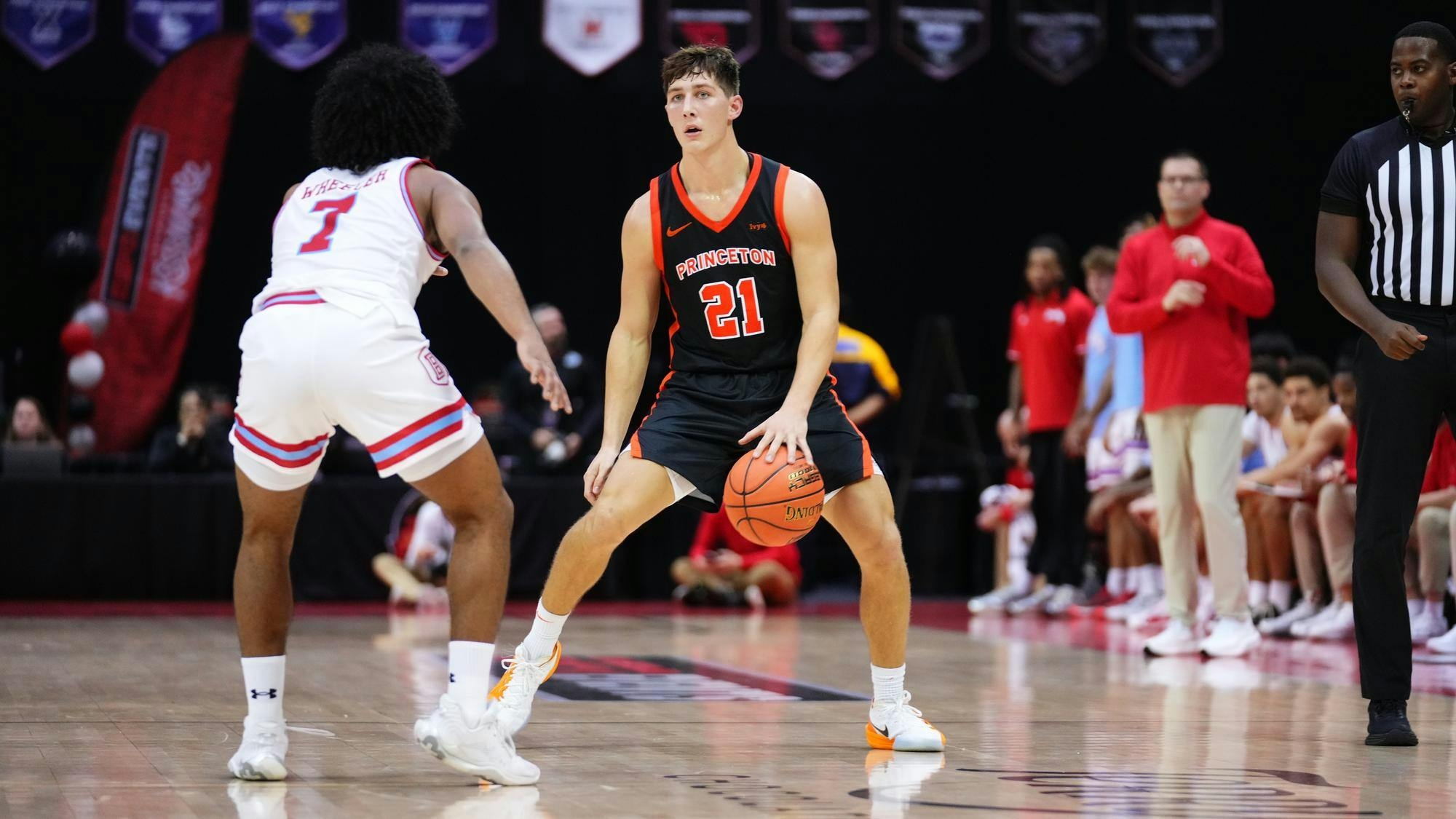 A Princeton basketball player in a black No. 21 jersey dribbles while being guarded closely by a defender in white on the basketball court.
