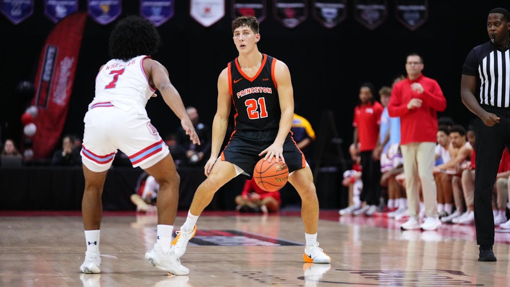 A Princeton basketball player in a black No. 21 jersey dribbles while being guarded closely by a defender in white on the basketball court.