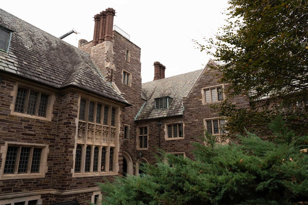 A gray-brick building stands in the background under a cloudy sky. An evergreen tree is in front of the building.