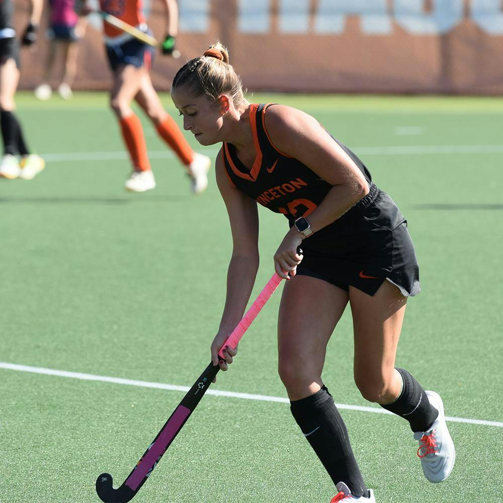 Woman in black and orange uniform holds pink stick towards the ground.