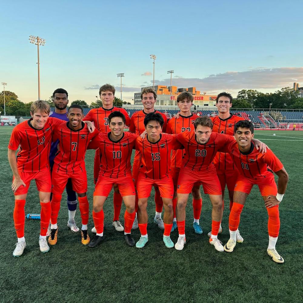 Several men in orange and black soccer uniforms stand with their arms over each other.