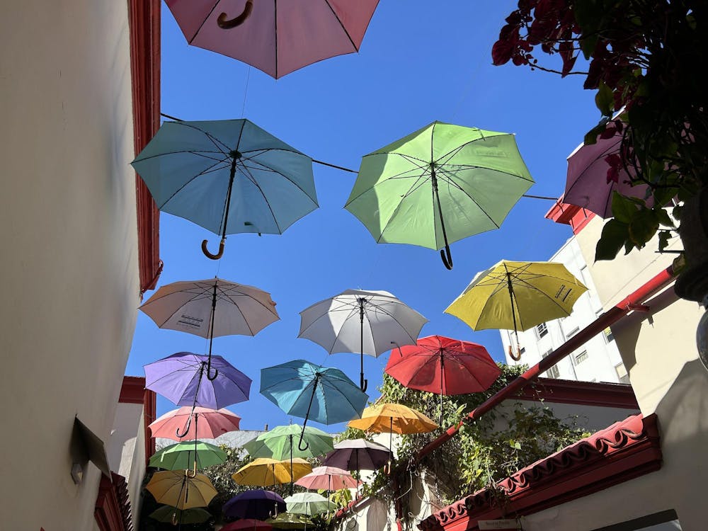 A canopy of green, blue, purple, and yellow umbrellas strung between buildings.  
