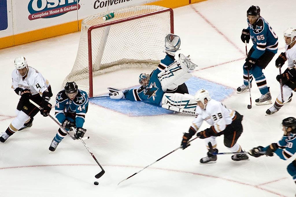 An Ice Hockey between San Jose Sharks vs. the Anaheim Ducks. Blue and white jersey wearing players play on white ice.