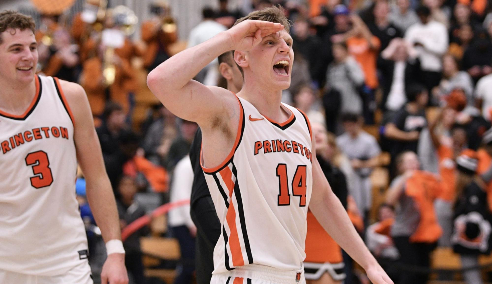 male basketball player salutes and yells while teammate smiles at him from behind