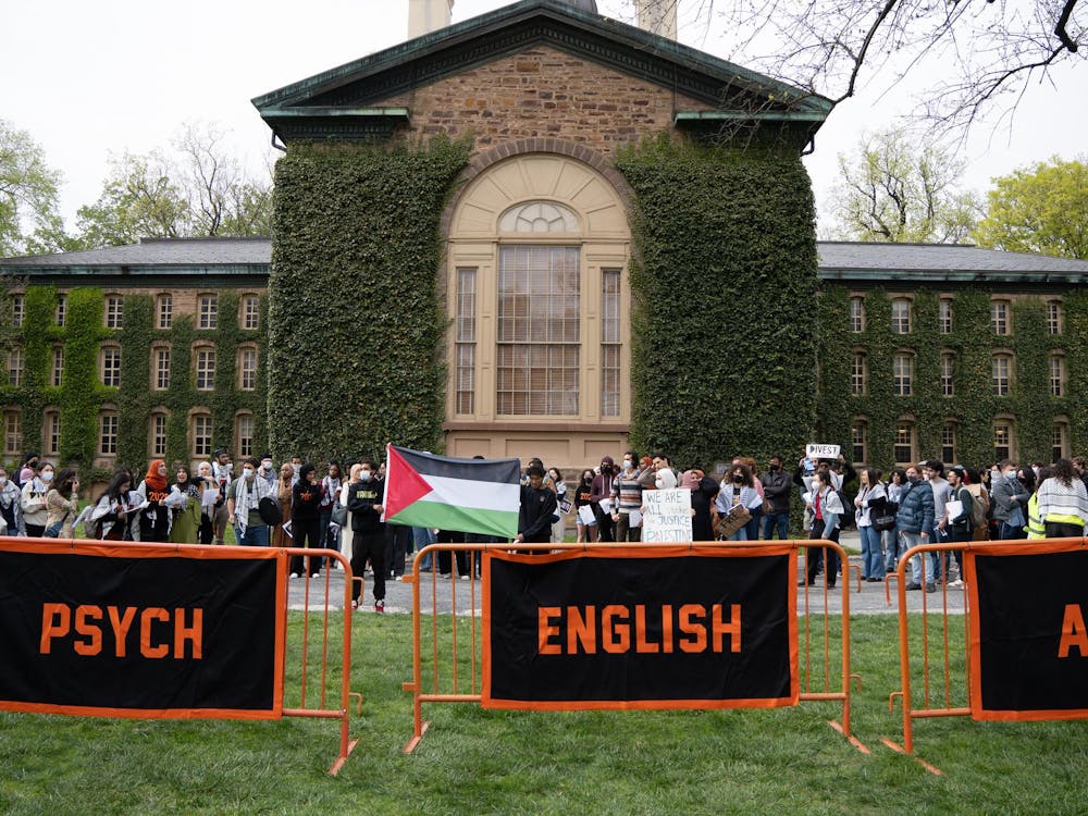 A group of protestors in stand in front of an ivy-covered building, behind three orange and black banners.