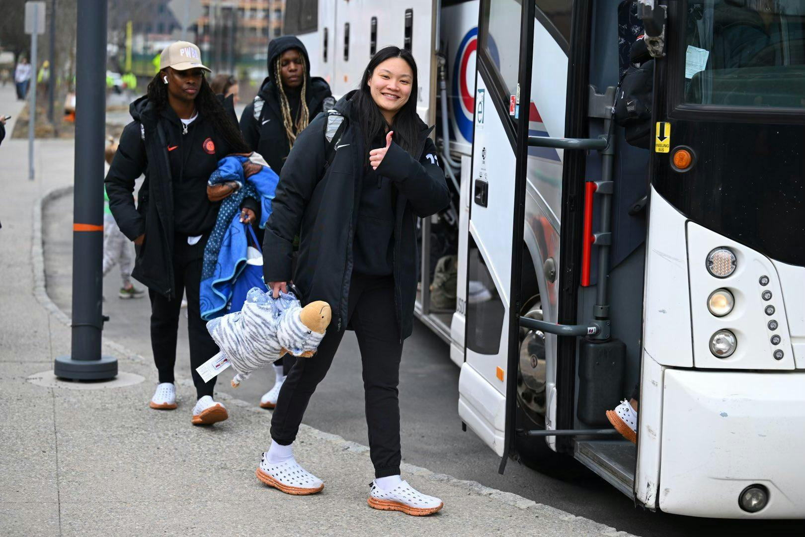 Three girls wearing black Princeton Athletics coat boarding a Coach bus on a residential street. 