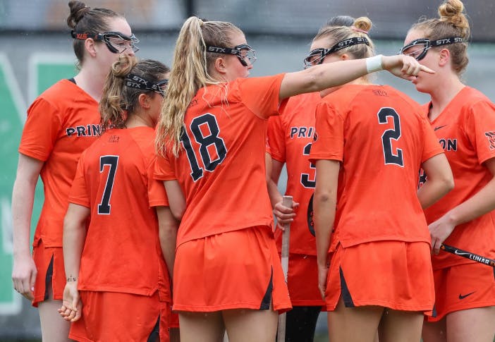 Photo of women’s lacrosse players wearing orange in a huddle