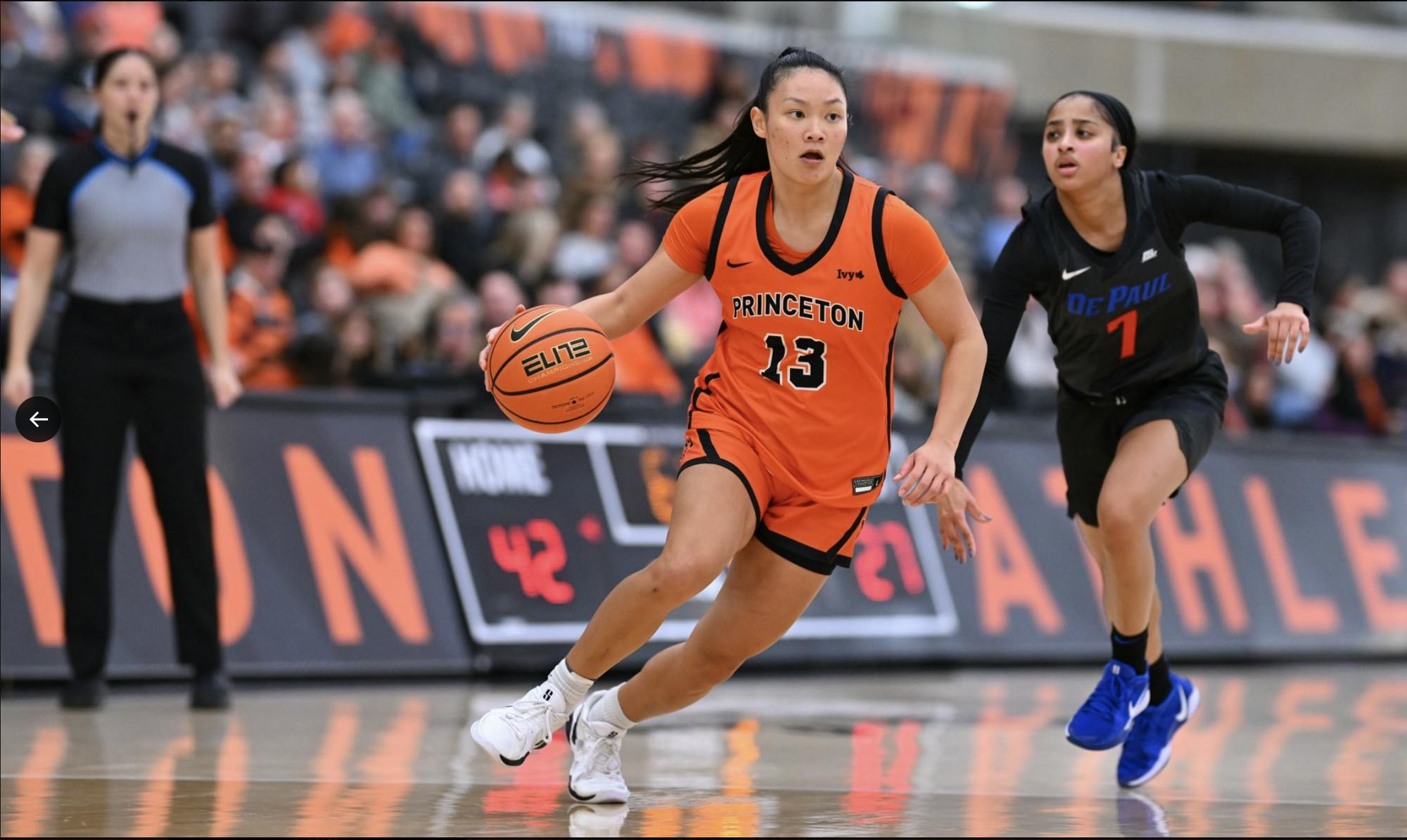 A woman in an orange basketball jersey dribbles the basketball past a defender wearing black.